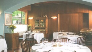 Un comedor con varias mesas dispuestas para una comida, paneles de madera y vista a zonas verdes.