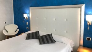 Habitación de hotel con una cama grande, una silla blanca y una pared azul decorativa.