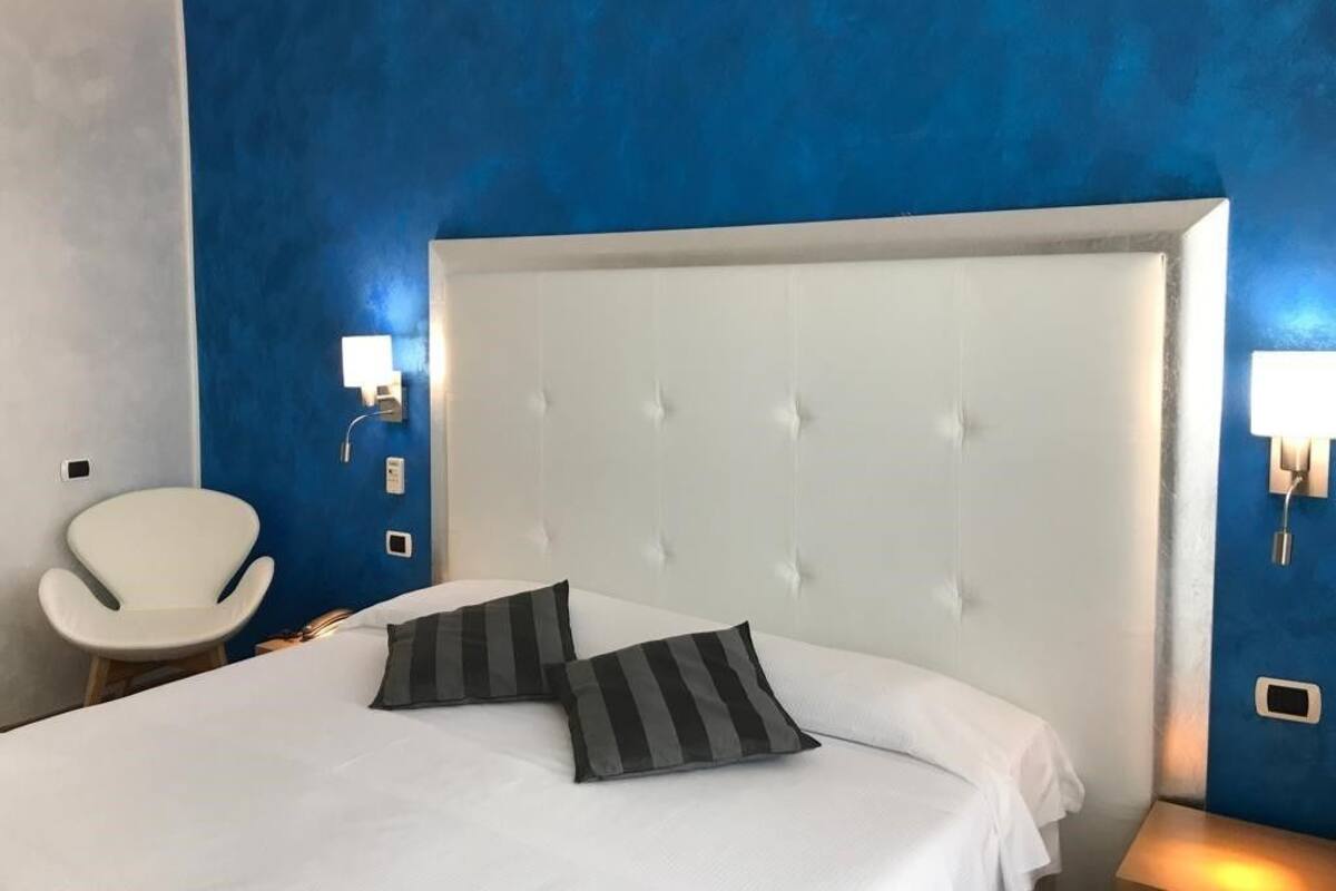 A hotel room with a large bed, a white chair, and a blue accent wall.