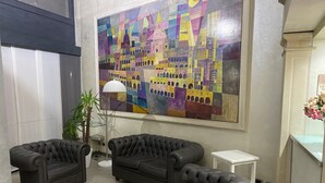 Un vestíbulo con dos sofás de cuero negro, una lámpara de pie y un cuadro abstracto grande en la pared.