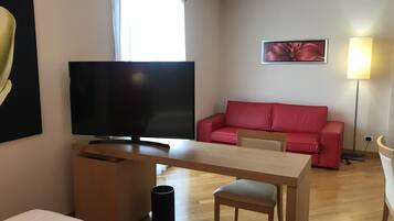 A modern living room with a flat-screen TV, a red sofa, a wooden coffee table, and a lamp.