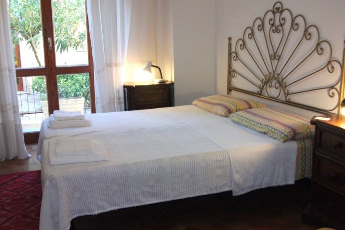 A neatly made bed with a metal headboard, a bedside lamp, and a window with curtains.