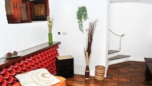 A room with a brick floor, a red and white patterned wall, a wooden bench, a small table with a vase, and a staircase leading to an upper level. - Solemare b&b - Apartments Alghero (Alghero)