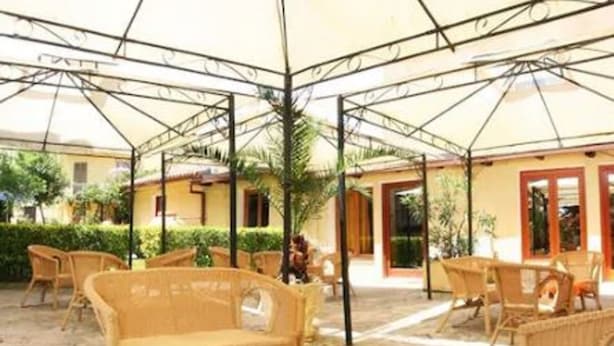 An outdoor seating area with wicker furniture and a table, surrounded by a covered patio with a metal frame and a yellow building in the background. - Solemare b&b - Apartments Alghero (Alghero)