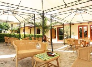 An outdoor seating area with wicker furniture and a table, surrounded by a covered patio with a metal frame and a yellow building in the background. - Solemare b&b - Apartments Alghero (Alghero)