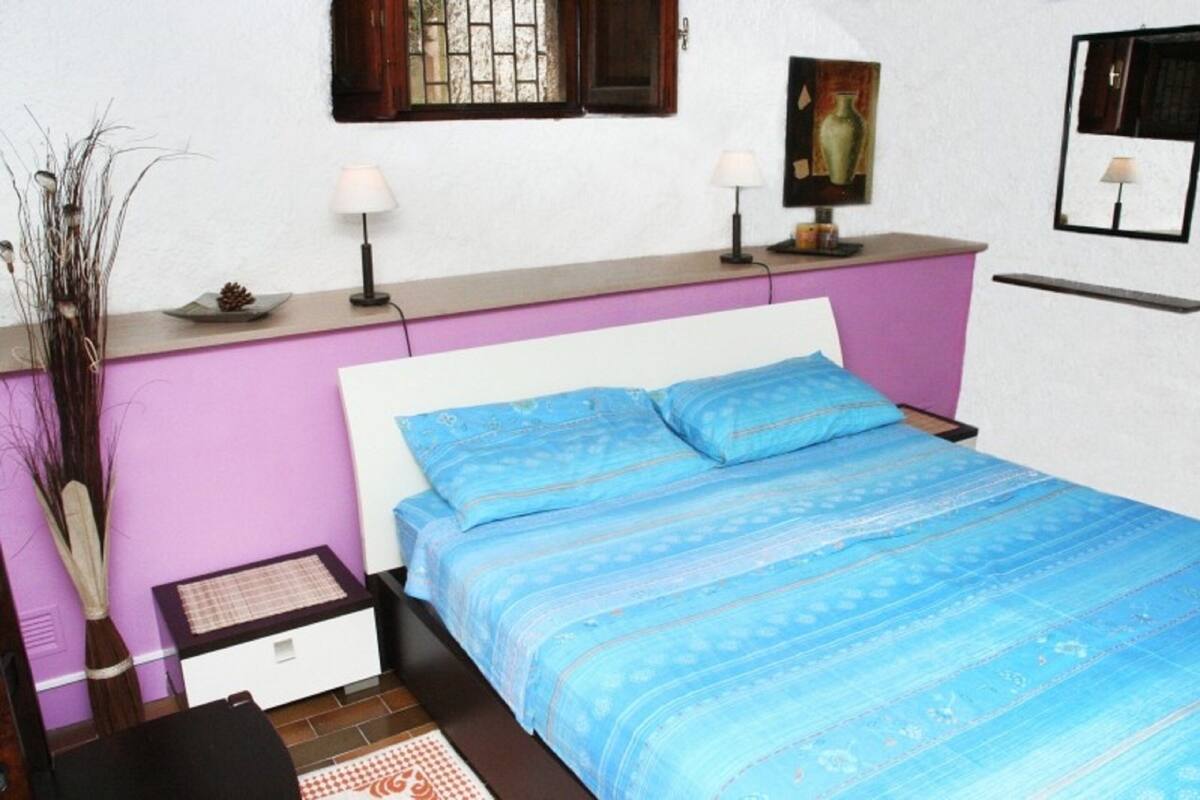 A bedroom with a bed, bedside lamps, a small table, and a vase on the nightstand.
