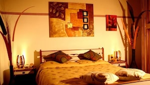A neatly made bed with a patterned bedspread, two bedside tables with lamps, and a wall art piece above the bed. - Solemare b&b - Apartments Alghero (Alghero)