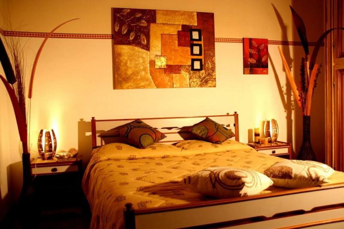 A neatly made bed with a patterned bedspread, two bedside tables with lamps, and a wall art piece above the bed.