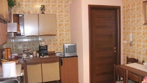 A compact kitchen with a refrigerator, a small television, and a dining area with a table and chairs. - Solemare b&b - Apartments Alghero (Alghero)