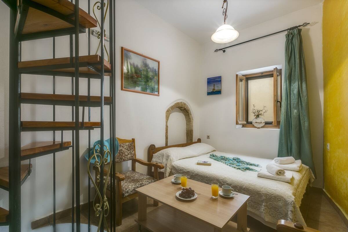 A bedroom with a bed, a chair, a table with breakfast items, a window with curtains, and a staircase.