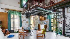 A spacious living area with a dining table, chairs, and a sofa. There is a staircase with a wooden railing leading to an upper level. - Ifigenia Rooms & Studios (Chania)