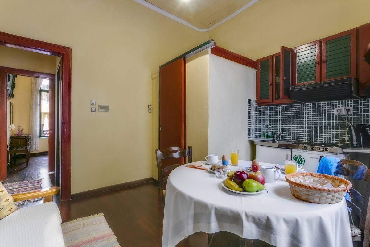 A dining area with a table set for breakfast, including fruits, beverages, and a basket.