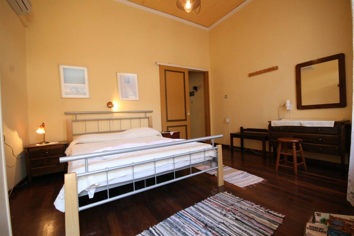 A bedroom with a bed, bedside table, lamp, wooden floor, and a mirror on the wall.
