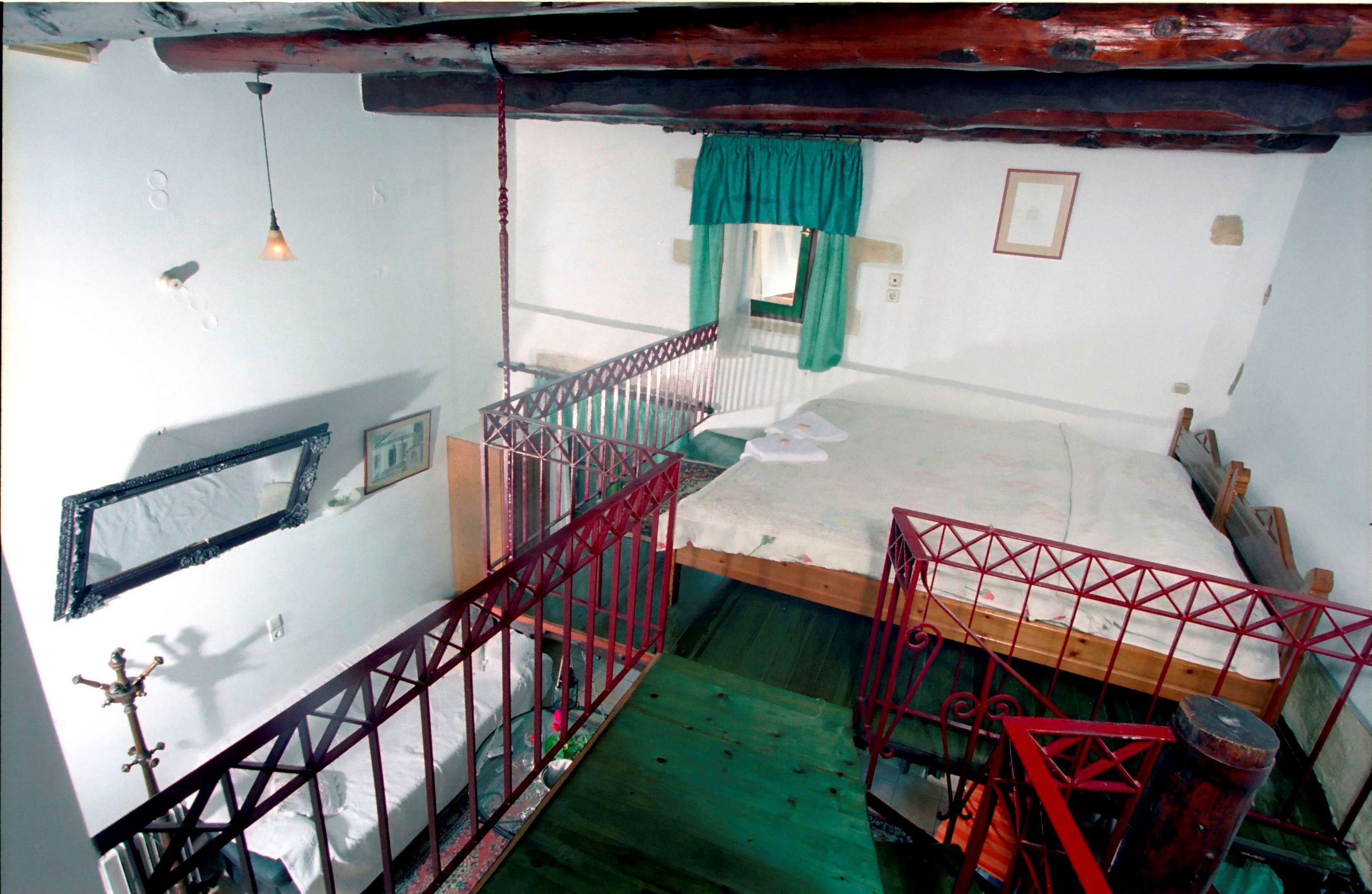 Una habitación pequeña y rústica con una cama individual, una escalera de madera, un ventanal con cortina y un espejo en la pared.