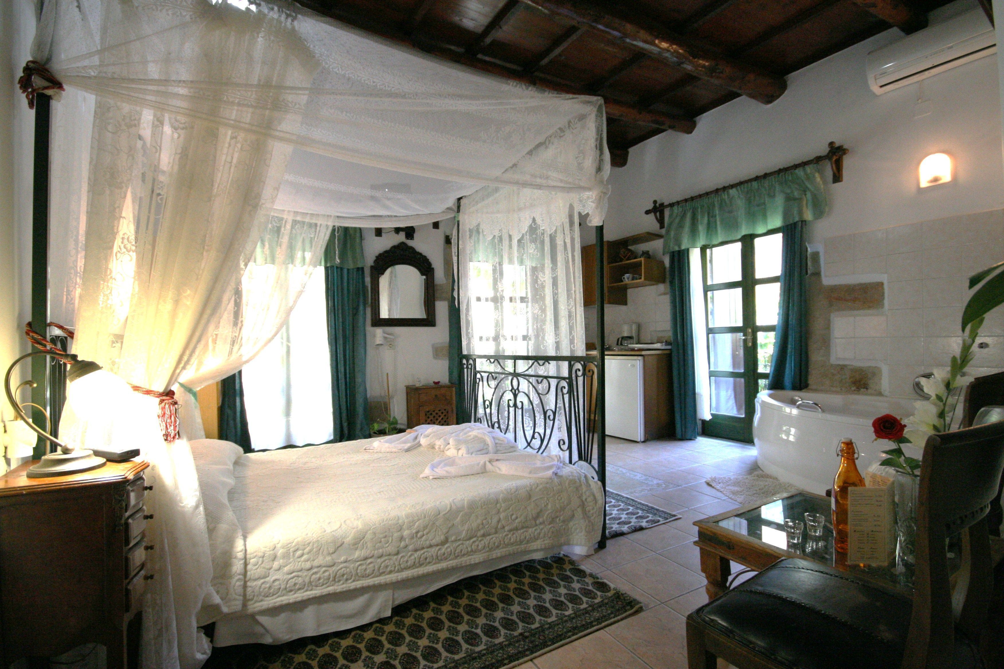 Une chambre à coucher comprenant un lit, une table de chevet, une lampe, une fenêtre avec des rideaux, un miroir, une salle de bain avec une baignoire et une chaise.