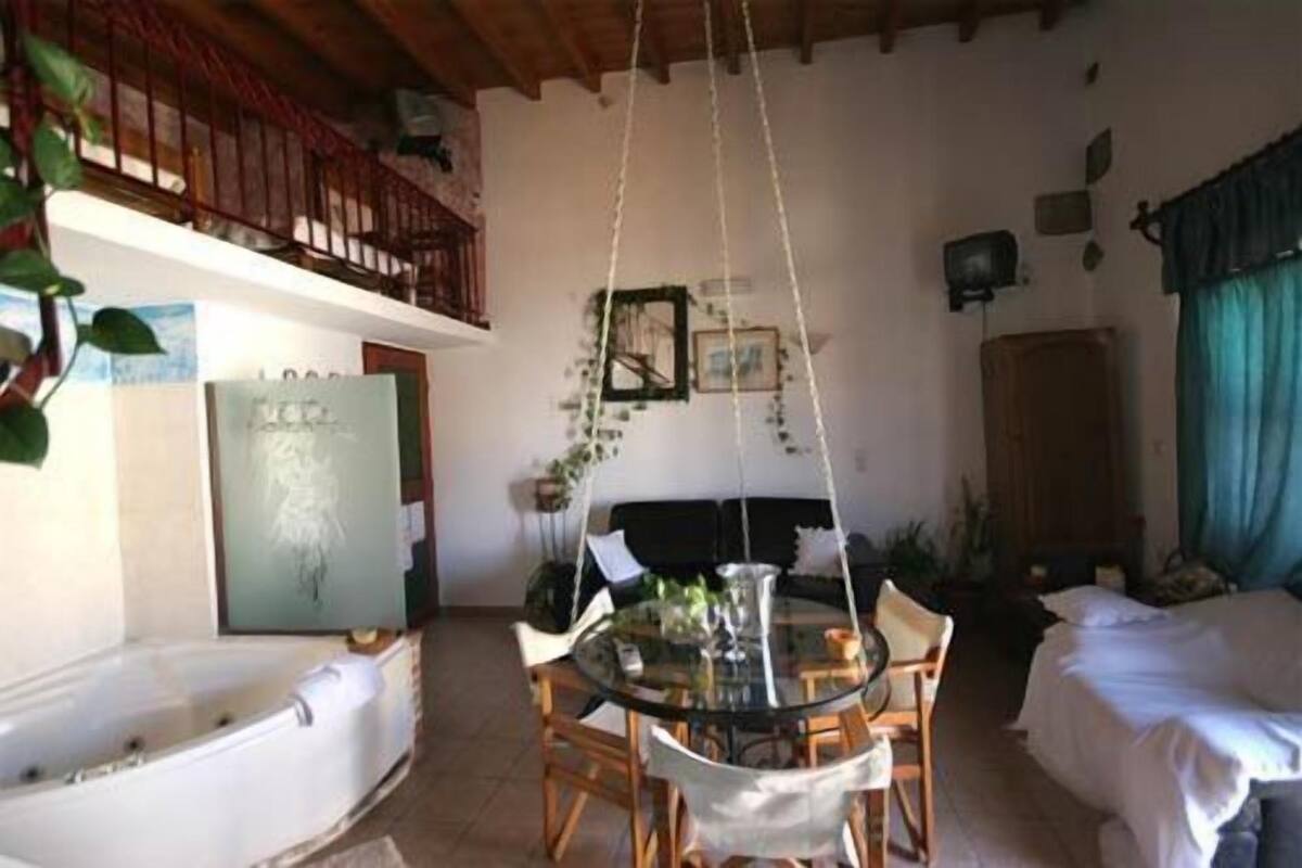 A room with a glass table, chairs, a bed, a bathtub, and a balcony with a railing.