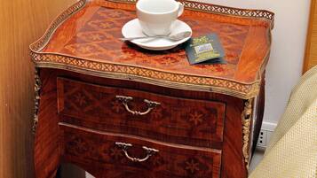 A wooden side table with a white cup and saucer, a spoon, and a booklet.