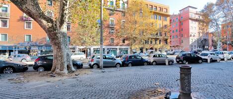 A cobblestone street with parked cars and multi-story buildings in the background.