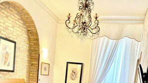 Camera d'hotel con un letto grande, una testiera in legno, un lampadario, una scrivania in legno, una sedia e una finestra con tende.