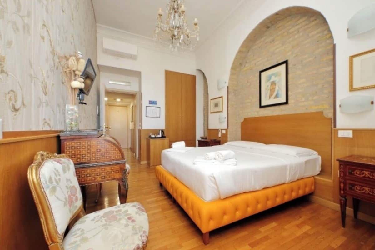 A hotel room with a large bed, wooden furniture, a chandelier, and a brick wall.