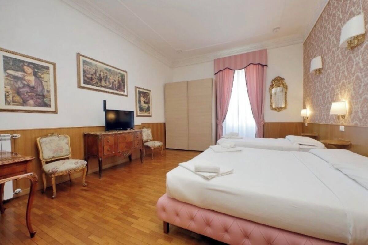 A hotel room with a bed, a desk, a chair, a television, and artwork on the walls.