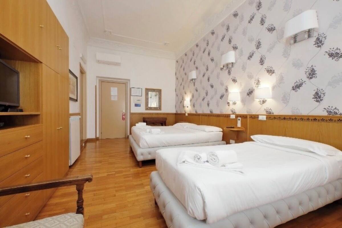 A hotel room with two beds, wooden furniture, a television, and wall-mounted lamps.