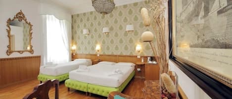 A hotel room with two beds, a chandelier, a mirror, and a framed picture on the wall.