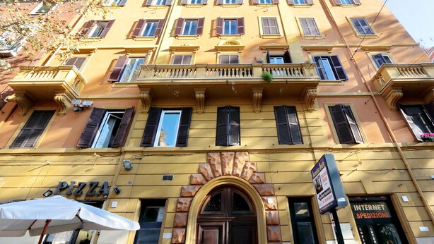 Un edificio a più piani con facciata gialla, con una pizzeria visibile al piano terra e un cartello per servizi internet sulla destra.