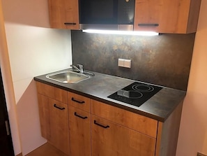 A compact kitchen with a stainless steel countertop, two sinks, a built-in stove, and wooden cabinets.