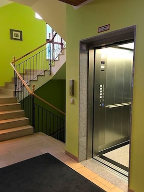 A staircase with a handrail, a carpeted landing, and an elevator with a control panel.