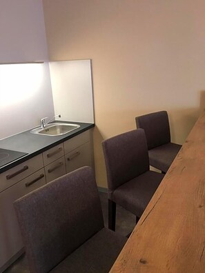 A small kitchenette with a sink and cabinets, two chairs, and a wooden table.