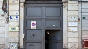 Fachada de edificio con una amplia entrada arqueada, un balcón con barandilla decorativa y varios carteles, incluyendo uno de prohibido estacionar y números de habitación.