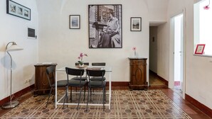 Un comedor con una mesa, sillas y un piso con diseño. Hay cuadros en las paredes y un cuadro grande sobre la mesa.