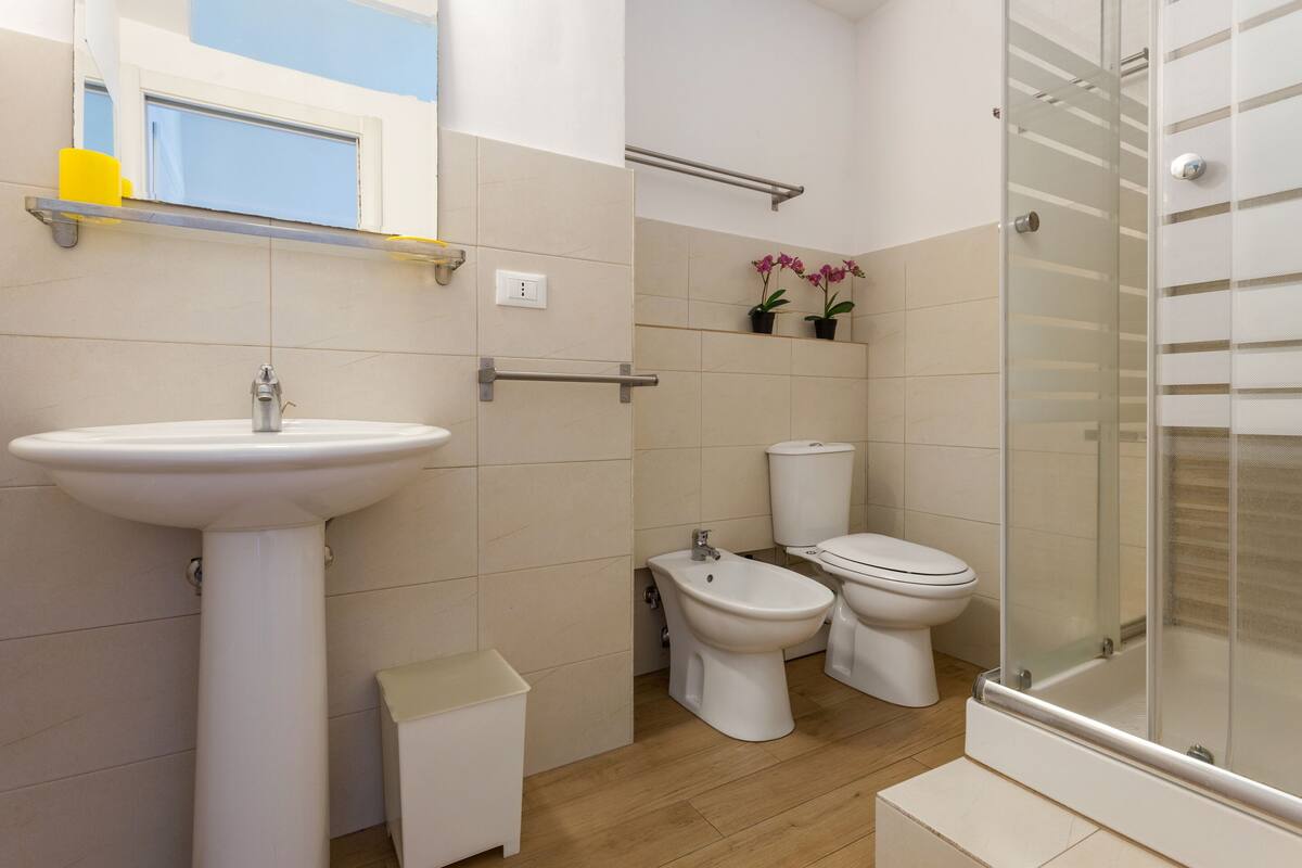 Une salle de bain équipée d’un lavabo sur colonne, d’un bidet, de toilettes et d’une douche à parois de verre.