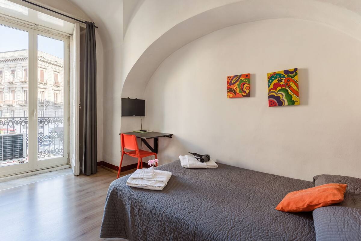 Une chambre d’hôtel avec un lit, un bureau, une chaise et deux tableaux accrochés au mur.