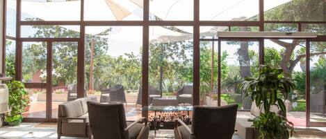 Un espacio interior amplio con ventanas grandes, una disposición de asientos con sillas y una mesa, y una planta en maceta.