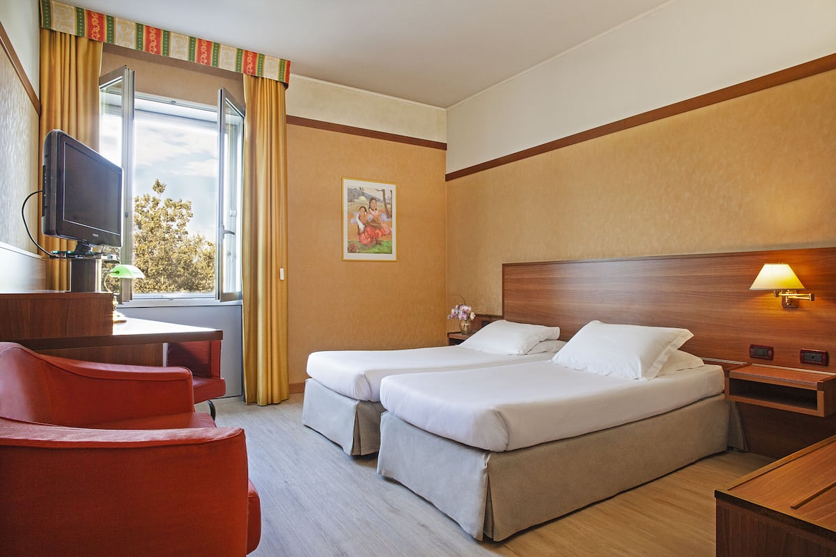 Een hotelkamer met twee bedden, een bureau met een televisie, een rode stoel en een raam met gordijnen.