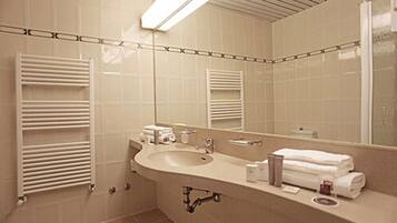 A modern bathroom with a large sink, mirror, towel rack, and a shower area.