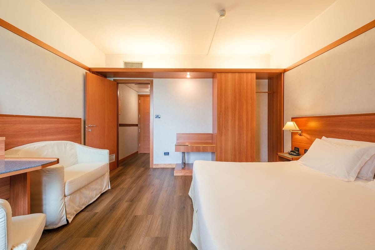 Een hotelkamer met een bed, een bureau en een stoel. Er is een badkamer met een wastafel en spiegel.