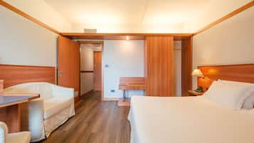 A hotel room with a bed, a desk, and a chair. There is a bathroom with a sink and mirror.