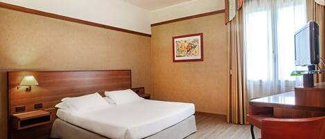 A hotel room with a bed, a desk with a television, a lamp, and a painting on the wall.