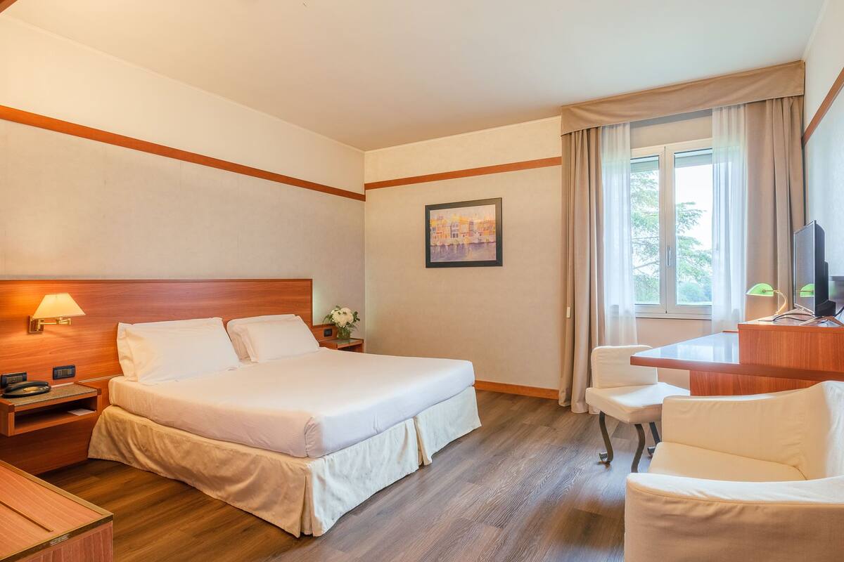 Een hotelkamer met een bed, een bureau, een stoel, een televisie en een schilderij aan de muur.