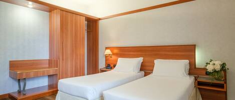 Habitación de hotel con dos camas, una mesita de noche de madera y una lámpara de pared.