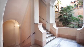 A staircase with a handrail, leading to an upper floor. There is a window with a view of buildings and a palm tree outside. - Pantheon Inn (Rome)