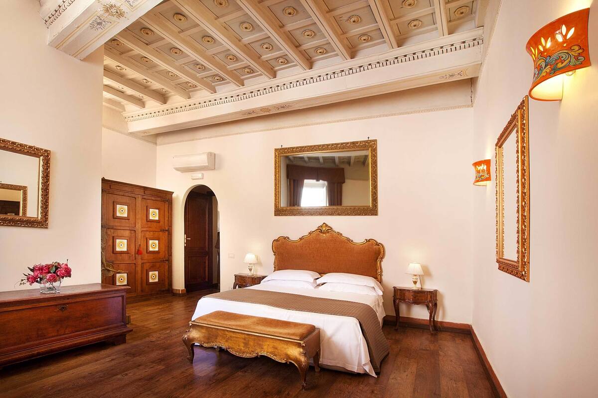 A spacious bedroom with a large bed, wooden wardrobe, and a ceiling with intricate designs.