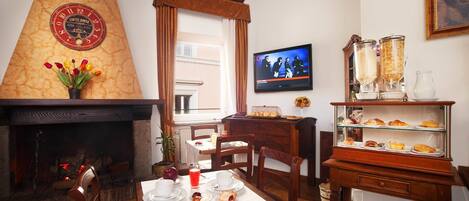 A dining area with a fireplace, a television, and a display case with pastries.
