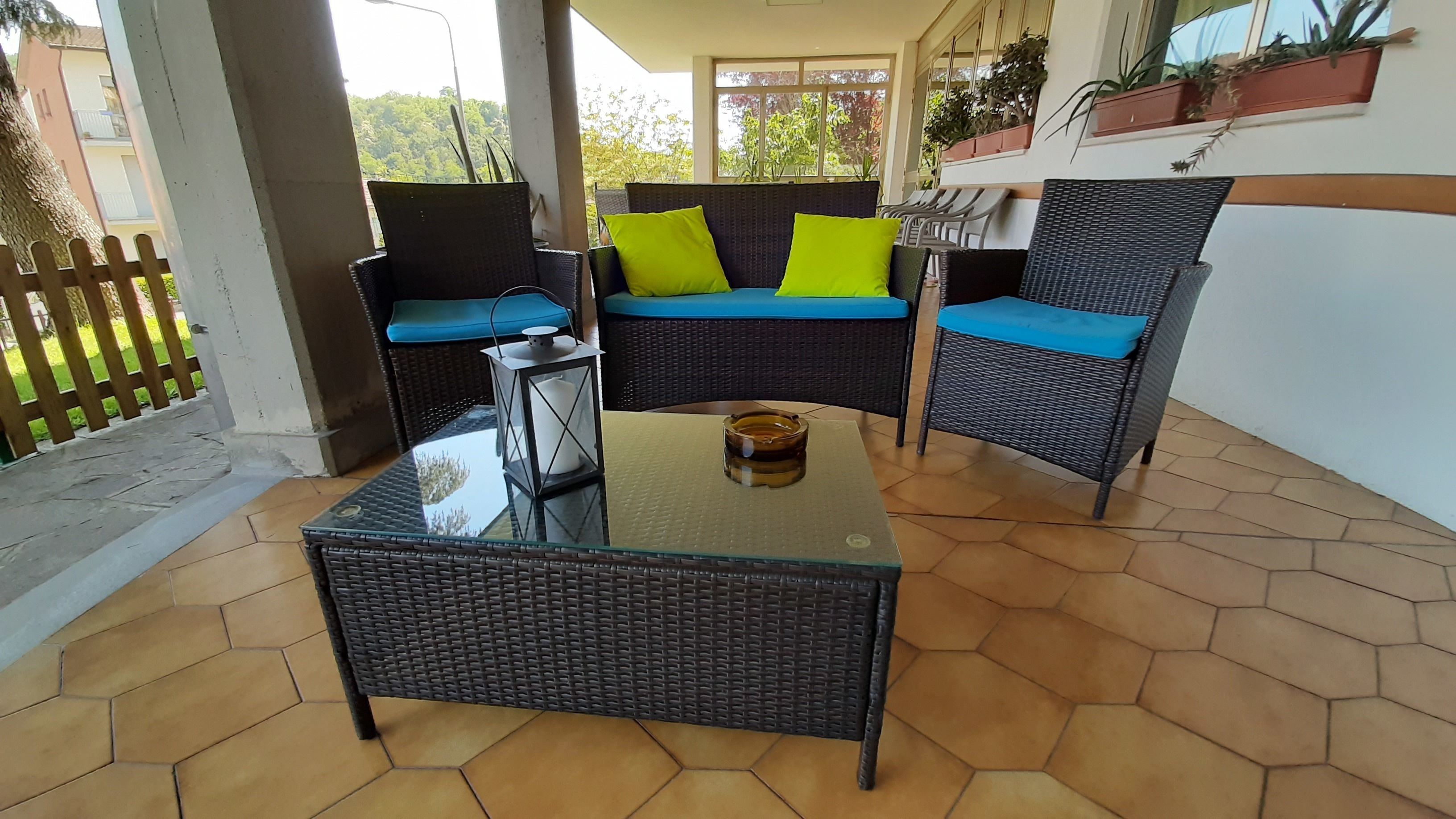 A patio area with wicker furniture, a glass table, and potted plants.