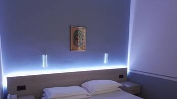 A hotel room with a bed, bedside tables, and a wall-mounted light fixture.