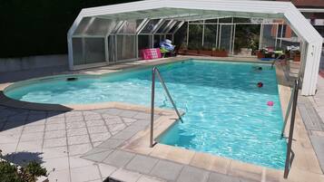 Piscina com cobertura de vidro, deck revestido e plantas em vasos.