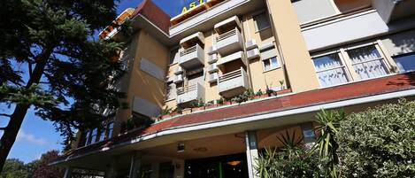 Un hotel de varios pisos con una entrada destacada, balcones y una variedad de plantas en macetas.